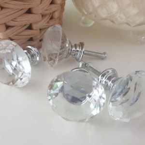 May include: Three clear crystal cabinet knobs with silver metal bases. The knobs have a faceted design.