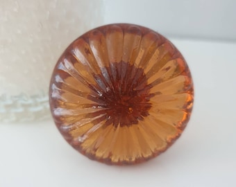 May include: A round, amber-colored glass knob with a textured, sunburst design.