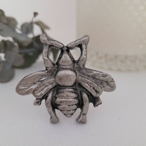 May include: A silver metal bee figurine with detailed wings and a textured body.