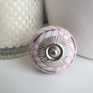 Op de afbeelding: Een roze keramische knop met een wit en zwart bloemenpatroon en een zilveren metalen midden.