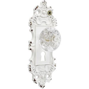 Può includere: Maniglia per porta bianca e ornata con pomello in vetro trasparente. La maniglia ha una finitura anticata con accenti marroni e una serratura. Il design è di ispirazione vintage, con volute decorative.
