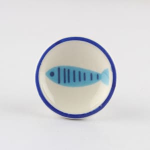 Op de afbeelding: Een klein wit keramiek schaaltje met een blauwe rand en een blauw en lichtblauw visontwerp.