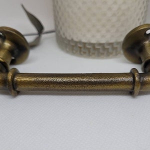 Peut inclure: Une poignée de tiroir en métal doré avec un design de tuyau. La poignée a une forme arrondie et est conçue pour être montée sur une armoire ou un tiroir.