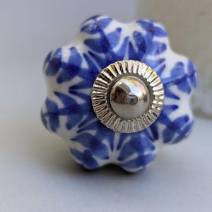 May include: Blue and white ceramic knob with a silver metal center. The knob has a floral pattern and a slightly bumpy texture.