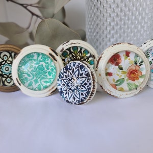 May include: Six decorative cabinet knobs with various floral and geometric patterns. The knobs are white with a distressed finish and feature blue, green, and gold accents.