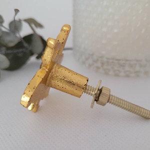 May include: Gold metal cabinet knob with a decorative floral design. The knob has a screw and a washer.