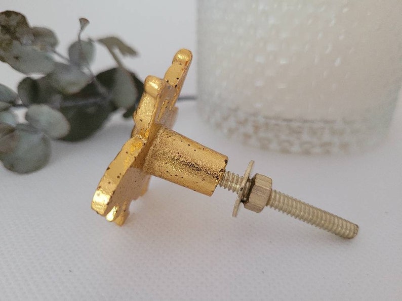 May include: Gold metal cabinet knob with a decorative floral design. The knob has a screw and a washer.