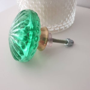 May include: A green glass door knob with a brass base and a silver screw. The knob has a textured, rippled surface.