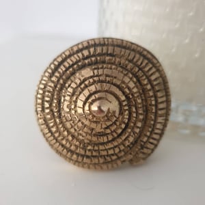 以下が含まれることがあります： 同心円と盛り上がった中心部を持つ円形のデザインが施された金色の金属製のリングです。