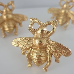 Puede incluir: Tres anillos de servilleta de abeja dorada. La abeja está detallada con una superficie texturizada y tiene un diseño tridimensional.