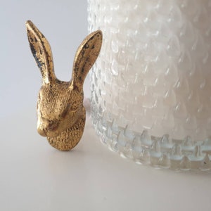 May include: A gold-colored rabbit head figurine with a detailed design. The figurine is on a white surface.