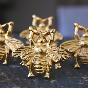 May include: Five gold bee-shaped decorative objects. The bees are detailed with raised wings and legs.