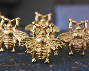 May include: Five gold bee-shaped decorative objects. The bees are detailed with raised wings and legs.