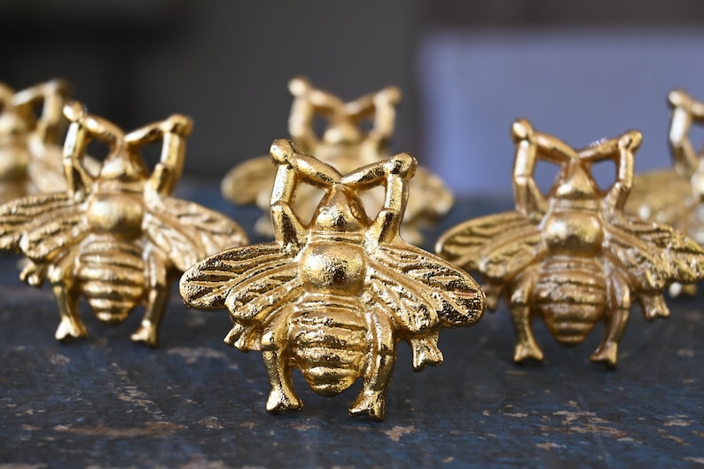 May include: Five gold bee-shaped decorative objects. The bees are detailed with raised wings and legs.
