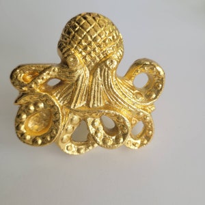 Può includere: Una statuetta di polpo dorata con una superficie testurizzata. Il polpo ha otto tentacoli e una testa dettagliata.