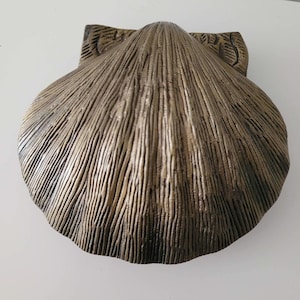 May include: A gold-coloured seashell shaped trinket box with a detailed textured surface.