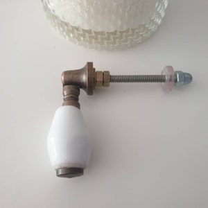 Può includere: Pomo per porta in ceramica bianca con base in ottone e vite in metallo. Il pomo è fissato a un'asta metallica con una rondella e un dado.