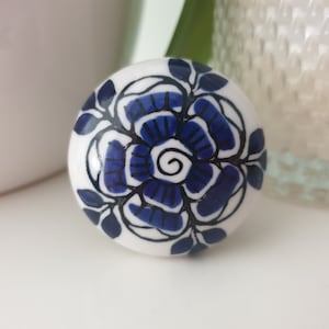 May include: A white ceramic knob with a blue and black floral design. The knob features a large, stylized flower with intricate details.
