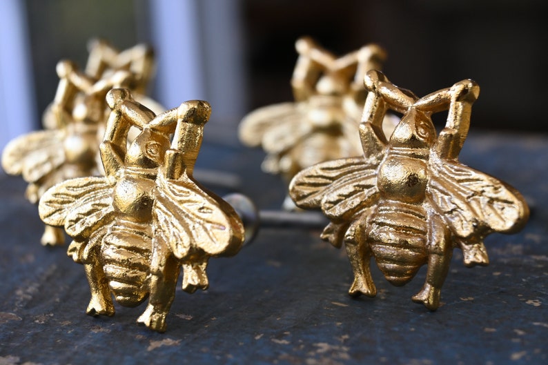 May include: Four gold bee-shaped drawer pulls with intricate details. The bee's wings, legs, and body are all sculpted with a realistic design.