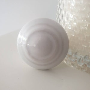 Peut inclure: Bouton de porte en céramique blanche avec un design circulaire et une finition lisse et brillante.