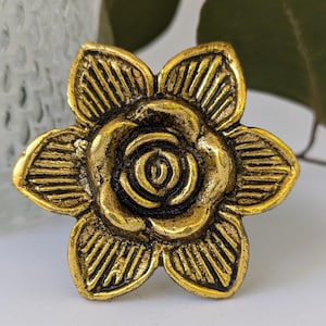 May include: A gold-toned metal flower-shaped drawer pull with a raised rose design.