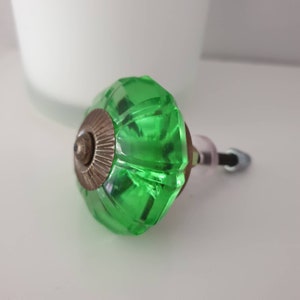 May include: A green glass cabinet knob with a brass base. The knob has a faceted design and a rounded shape.