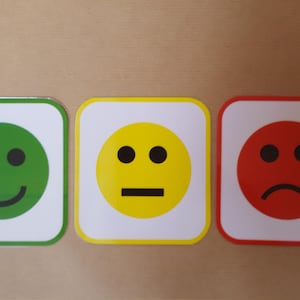 May include: Three square emoji signs with rounded corners. The first is green with a smiling face, the second is yellow with a neutral face, and the third is red with a frowning face. Each emoji has a white border.