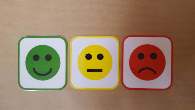 May include: Three square emoji signs with rounded corners. The first is green with a smiling face, the second is yellow with a neutral face, and the third is red with a frowning face. Each emoji has a white border.