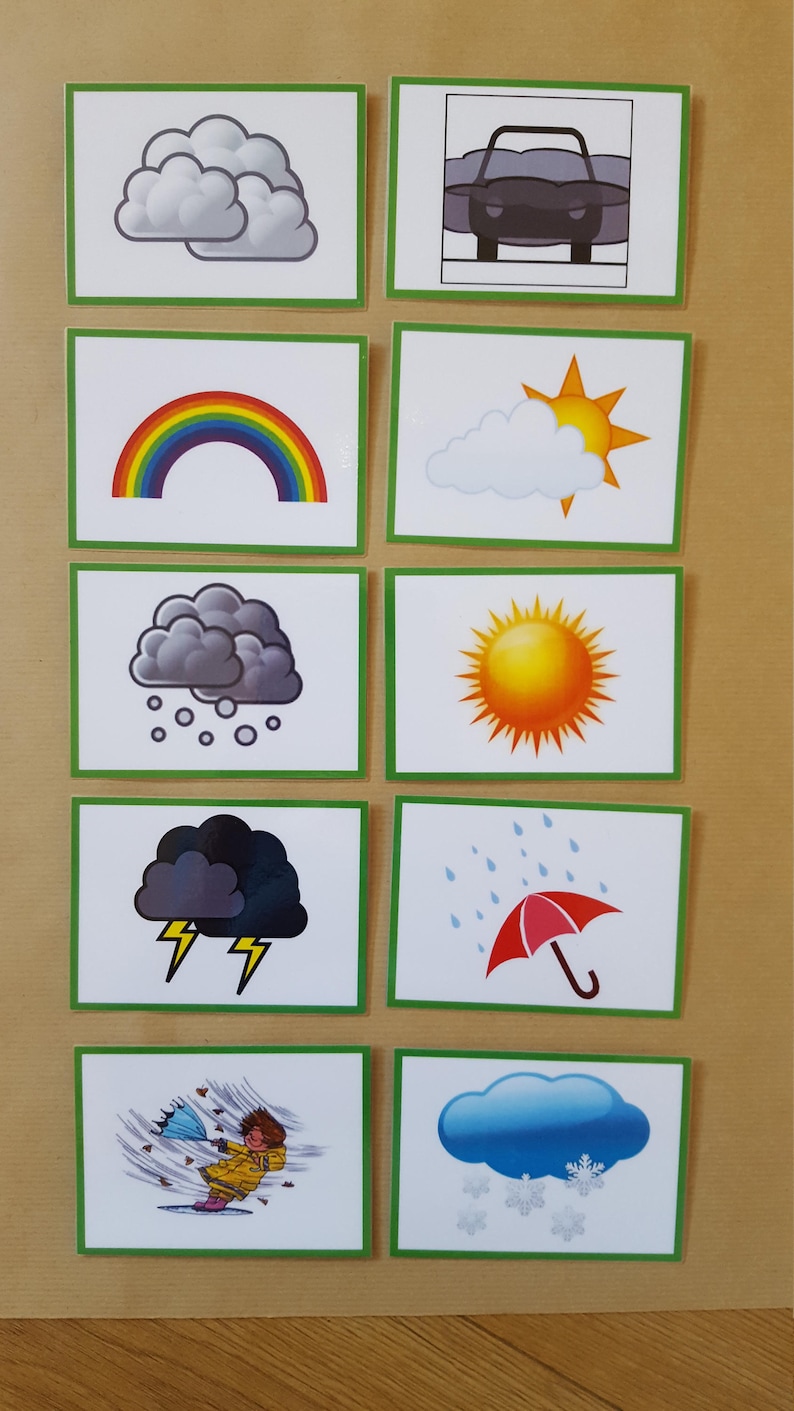 May include: A collection of weather-themed flashcards. Each card features a different weather condition, including clouds, a rainbow, rain, snow, and a sunny day. The cards have a green border and are arranged on a light brown surface.
