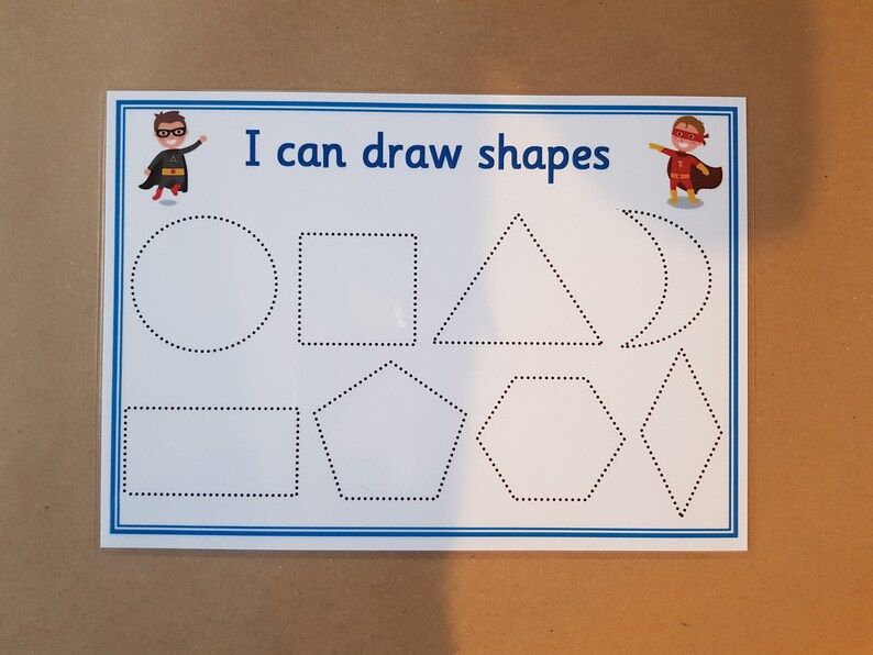 May include: White educational worksheet with blue border featuring the text "I can draw shapes" and illustrations of shapes. Includes a circle, square, triangle, and other shapes. Superhero illustrations are in the corners.