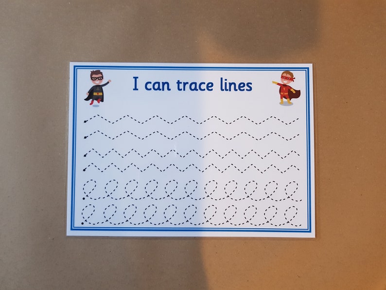 May include: A white educational tracing worksheet with a blue border. The text "I can trace lines" is at the top. The worksheet features dotted lines in various patterns, including zigzags and loops, for tracing practice. Superhero illustrations are on each side of the text.
