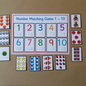 May include: A number matching game with cards featuring colorful numbers 1-10 and corresponding images like apples, soccer balls, and teddy bears. The game includes a white board with the text "Number Matching Game 1-10".