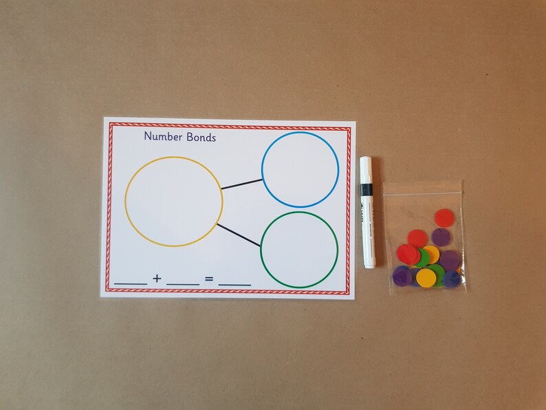 May include: A white educational number bonds worksheet with a red border, featuring three circles and the text "Number Bonds." Includes a white marker and a bag of colorful circular counters. Educational supplies.