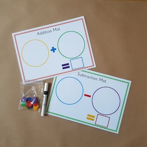 May include: Educational addition and subtraction mats. Each mat has a coloured border and includes circles for numbers and symbols. Includes a dry-erase marker and colourful counters.