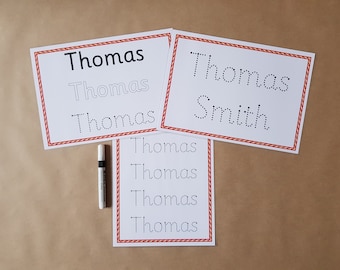 May include: White paper sheets with the name "Thomas" printed in various styles, including solid, dotted, and outlined. A black and white marker is also present. The sheets have a red border.