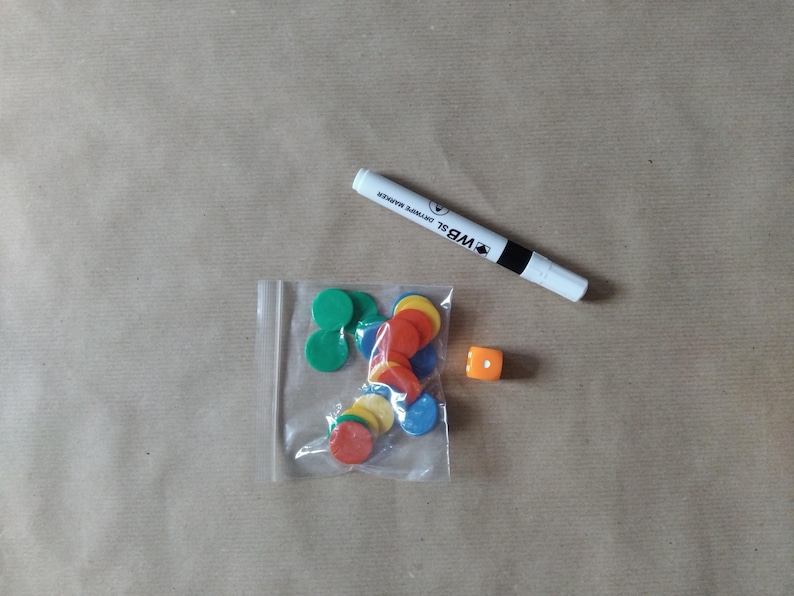 May include: A collection of colorful game pieces, including green, red, yellow, and blue circular tokens in a clear plastic bag, an orange die, and a white dry-erase marker with black accents.