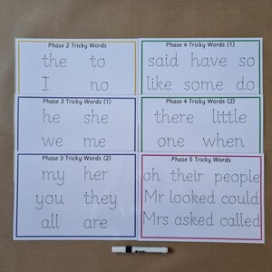 May include: Six white rectangular educational cards with dotted letters for tracing, organised by phase. The cards feature text including Phase 2 Tricky Words, Phase 3 Tricky Words, Phase 4 Tricky Words, and Phase 5 Tricky Words, accompanied by a dry erase marker.