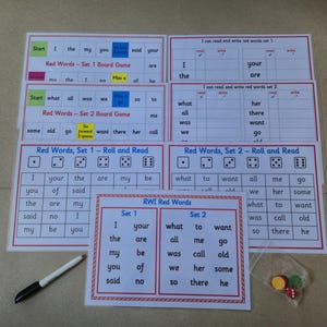 May include: Educational board games for learning red words. The image shows several laminated game boards with text, dice, and a pen. The games are designed for reading and writing practice, with sets for different word groups.