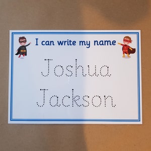 May include: A white educational learning board with a blue border and the text "I can write my name." The names "Joshua" and "Jackson" are printed in dotted lines for tracing. Superhero illustrations are on the top corners.
