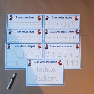 May include: Educational tracing activity sheets for kids. The set includes sheets for tracing lines, letters, shapes, numbers, and names. Each sheet has a blue border and features a superhero graphic. A marker is also included.