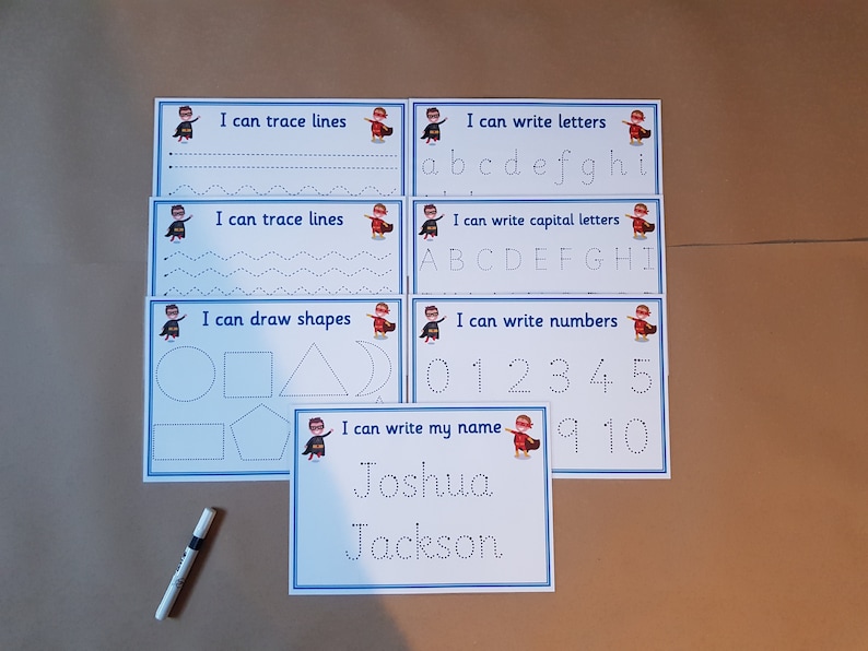 May include: Educational tracing activity sheets for kids. The set includes sheets for tracing lines, letters, shapes, numbers, and names. Each sheet has a blue border and features a superhero graphic. A marker is also included.