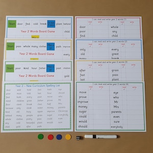 May include: Educational board game set for Year 2 pupils. Includes word games, spelling lists, and writing practice sheets. Features colourful game boards, magnetic game pieces, a die, and a marker. The text on the boards reads "Year 2 Words Board Game".