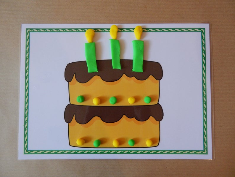 May include: A colorful birthday cake illustration with three candles. The two-tiered cake is yellow with brown frosting and decorated with green and yellow dots. The candles are green with yellow flames, set on a white background with a green border.