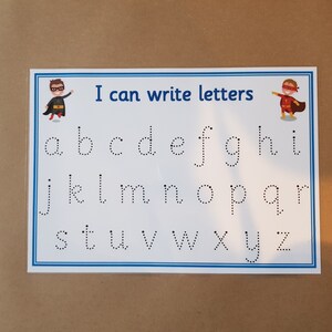 May include: A white educational chart with a blue border, featuring the lowercase alphabet in dotted lines for tracing. The text "I can write letters" is at the top, with superhero illustrations on each side. Ideal for early learning.