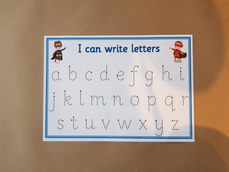 May include: A white educational chart with a blue border, featuring the lowercase alphabet in dotted lines for tracing. The text "I can write letters" is at the top, with superhero illustrations on each side. Ideal for early learning.