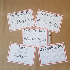 May include: Five white rectangular educational practice sheets with red patterned borders featuring black printed letters and numbers alongside dotted tracing versions. A single white dry-erase marker is positioned vertically between the sheets.