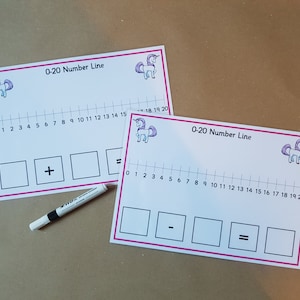 May include: Two white number line cards with pink borders, featuring a unicorn graphic and the text "0-20 Number Line." Each card has a number line, boxes for math problems, and a plus or minus sign. A white marker with a black cap is also present.