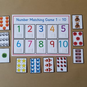 May include: A number matching game with cards featuring illustrations of apples, soccer balls, a green apple, stars, butterflies, clownfish, ladybugs, teddy bears, flowers, and red buses. The game board displays numbers 1-10.