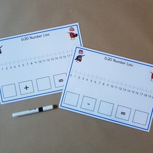 May include: Two white number line learning aids with blue borders, featuring a 0-20 number line, addition and subtraction symbols, and superhero graphics. A white marker is placed near the learning aids. The text "0-20 Number Line" is printed on the top.