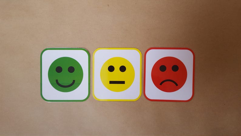 May include: Three square cards with smiley faces. The first card has a green smiley face with a smile, the second has a yellow face with a straight line for a mouth, and the third has a red face with a frown.